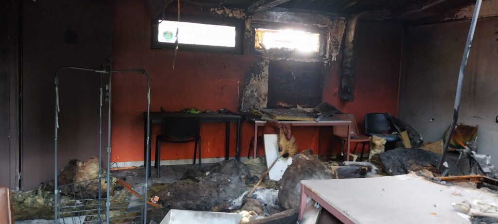 Interior calcinado del club-house tras el incendio: paredes ennegrecidas, aislante caído al suelo, mesas y sillas volcadas entre los escombros